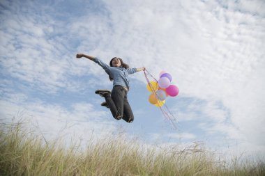 Renkli balon ile bulutlu ve mavi gök yeşil çayır üzerinde tutan mutlu kadın