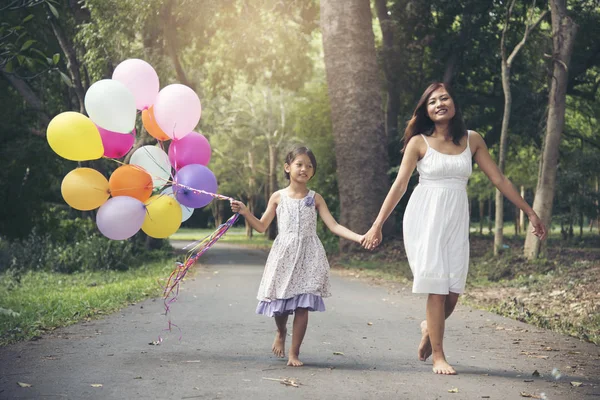 I love mom stay together on mother \'s day.Adorable cute girl holding balloons with mother walking on the road in the park. Family Concept.