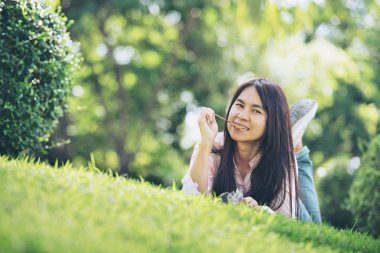 Güler yüz ile rahat genç güzel kadın parkta domuz sopa yeme keyfini çıkarın. İşten sonra dinlenmek için zaman. Horizontal.Blurred Background.Film etkisi.