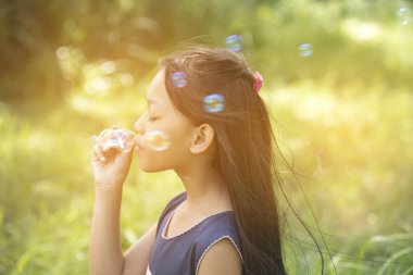 Cute girl play blowing bubble on playground with hard sun light. Little Kids enjoy and fun on play yard.