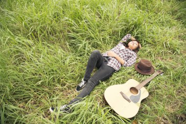 Woman laydown on green meadow after playing guitar on the beach with the blue sky. Travel Concept.