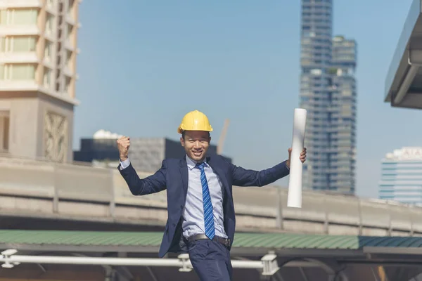 Successful engineer finishing project complete. holding fist and construction blue print in the air sign of victory. Success concept