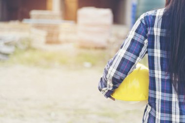 İnşaat alanında çalışan ve sarı başlıklı kaskı tutan kadın mühendisliği. İnşaat Konsepti.