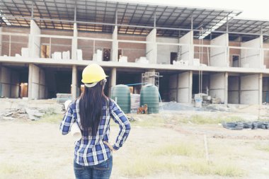 İnşaat alanında çalışan ve sarı başlıklı kaskı tutan kadın mühendisliği. İnşaat Konsepti.