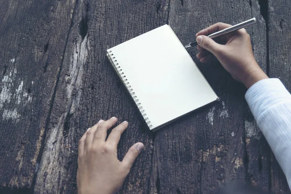 Close up woman hand writing on notebook. Woman writing on note paper diary on wooden table.