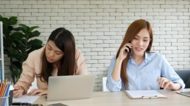 Mutlu girişimci Asyalı iş kadınları akıllı telefon pazarlığını yeni bir iş kurmak için kullanıyorlar. İki ortak akıllı telefonlardan iyi haberler alıyor. İş birliği yapan Asyalı kadın birlikte çalışıyor.