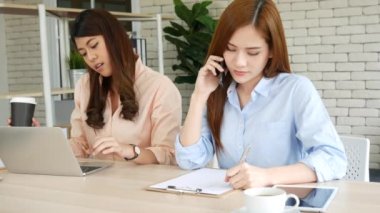 Mutlu girişimci Asyalı iş kadınları akıllı telefon pazarlığını yeni bir iş kurmak için kullanıyorlar. İki ortak akıllı telefonlardan iyi haberler alıyor. İş birliği yapan Asyalı kadın birlikte çalışıyor.