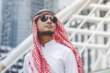 Modern şehirde duran yakışıklı modern Arap adam ofis dışında türban takıyor ve etnik tebessüm takıyor. Arap adam büyük şehirde yürürken yeni bir proje planlıyor. İş başarılı