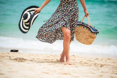 Yaz tatilinde sahilde bir kadın. Neşeli kadın sahilde oturmuş denize bakarken yazlık elbiseler ve hasır şapkalar giyiyor. Yazın tropik ada sahilinde açık hava çekimlerinde dinlenme zamanı..