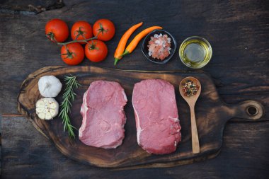 Manzaralı çiğ biftek malzemesi ahşap tahtada pişmemiş mutfak. Biftek, batı mutfağından taze et, biber, zeytin yağı, sarımsak, kırmızı biber, domates, tuz ve dışarıda parti için biberiye. Batı yemekleri konsepti