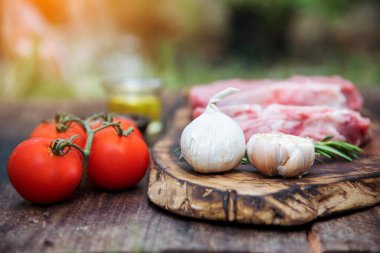 Manzaralı çiğ biftek malzemesi ahşap tahtada pişmemiş mutfak. Biftek, batı mutfağından taze et, biber, zeytin yağı, sarımsak, kırmızı biber, domates, tuz ve dışarıda parti için biberiye. Batı yemekleri konsepti