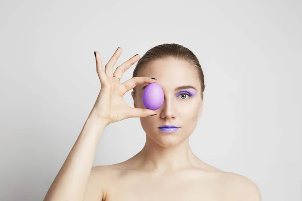 Studio záběr šťastné mladé ženy drží barevné velikonoční vajíčko před její oko. — Stock fotografie