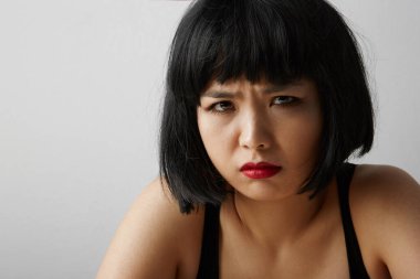 Beyaz arka planda poz veren kısa saçlı ve kızgın yüzlü genç Çinli kadın ön planda. İzole edilmiş.