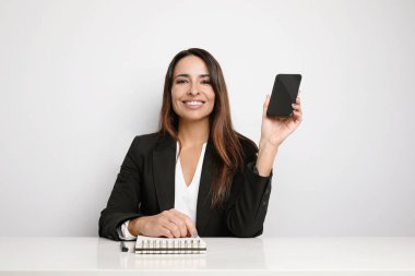 Beyaz duvarda poz veren ve akıllı telefonunu gösteren ofis sekreteri genç bayan. Ortak çalışma.