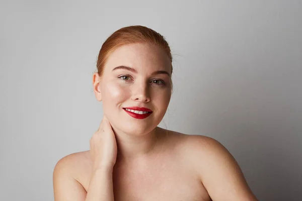Close-up portret van mooie jonge vrouw met naakte schouders en rode lippen kijkend naar de camera en lachend poserend op de grijze muur. geïsoleerd. — Stockfoto