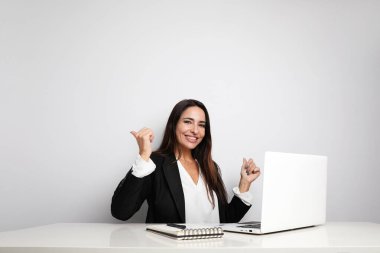 Ofis sekreteri genç bayan beyaz duvarda poz veriyor ve defterini gösteriyor. Ortak çalışma.