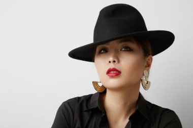 Beyaz arka planda poz veren ve siyah şapkalı Asyalı genç bir kadın. İzole edilmiş.