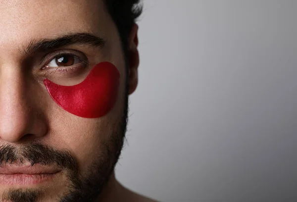 Retrato de perto de um jovem barbudo usando manchas vermelhas hidratantes. Luz do estúdio . — Fotografia de Stock