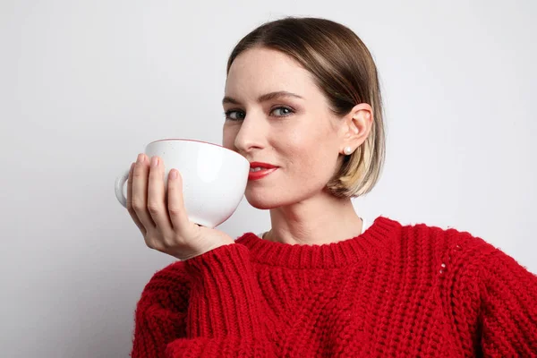 평범 한 옷을 입고 뜨거운 커피를 마시는 젊은 여성. 고립됨. — 스톡 사진