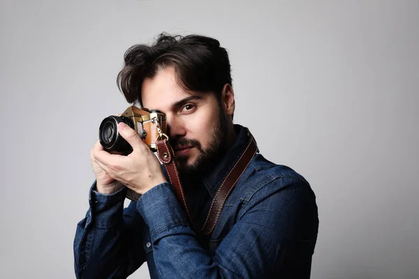 Joven barbudo hipster posando en el estudio y sosteniendo su cámara vintage . — Foto de Stock