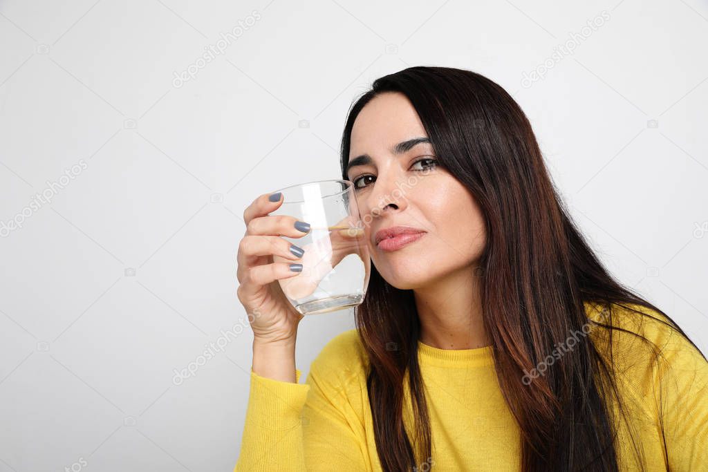Close-up portrait of young woman holding glass of water and looking at the camera. Healthy concept. Isolated.