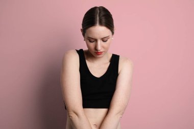 Siyah bluz giyen ve pembe arka planda poz veren bir kadın..