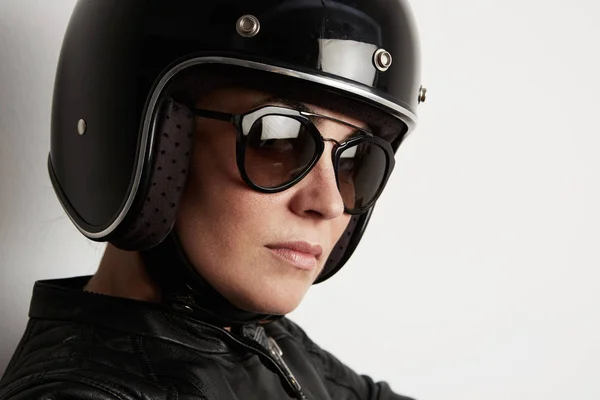 Close-up de mulher motociclista atraente posando na parede branca e vestindo capacete brilhante preto . — Fotografia de Stock