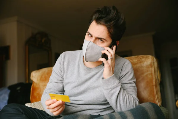 Young bearded man got a virus and using a medical mask. Making an order by phone.
