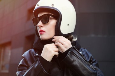 Beyaz kaskını ayarlayan motorcu kızın yakın plan portresi. Açık hava.. 