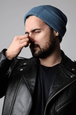 Genç sakallı hippi kötü kokudan muzdarip ve beyaz arka planda poz veriyor. Dikey.