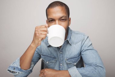 Beyaz duvara karşı kahve fincanı tutan siyahi bir genç..