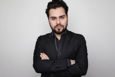 Beyaz arka planda poz veren takım elbiseli genç sakallı adam. Yatay.