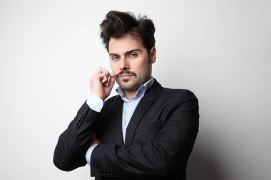 Beyaz arka planda poz veren takım elbiseli genç sakallı adam. Yatay.