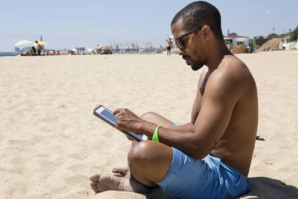Siyah bir erkek, boş zamanlarını mavi denize karşı oturarak ve tabletle çalışarak geçirdiği için mutlu.. — Stok fotoğraf