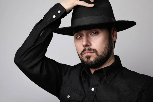 Portrait of bearded hipster wearing black hat and shirt looking at camera. — Stok Foto