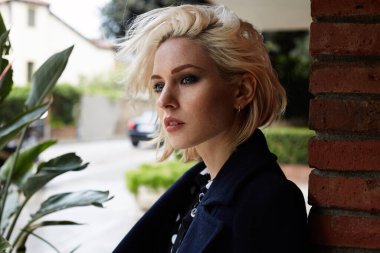 Sarışın, kıvırcık saçlı, zevkle gülümseyen güzel bir genç kız..