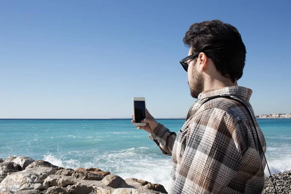 Jonge knappe man neemt een selfie en geniet van een zonnig weer op het strand. — Stockfoto