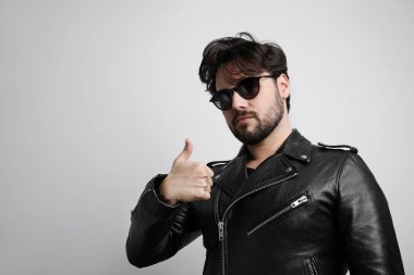 Bıyıklı, sakallı, sakallı, sakalsız, güneş gözlüklü, stüdyoda poz veren vahşi bir genç..