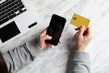Adamın el ele tutuşan akıllı telefonunun kopyası ve mermer yüzeyde kredi kartı ve dizüstü bilgisayarı kullanılıyor..