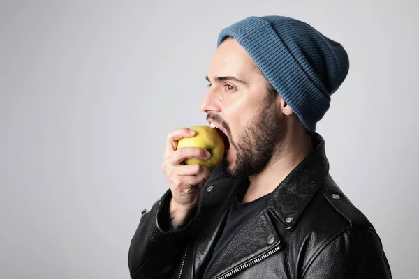 Przystojny i brodaty hipster noszący stylowy kapelusz na głowie i jedzący zielone jabłko. Brutalny mężczyzna z wąsami i brodą na nieogolonej brodatej twarzy. — Zdjęcie stockowe