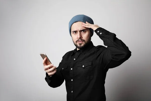 Jóképű és szakállas hipster visel stílusos kalap a fejét használja az okostelefon komoly arc. — Stock Fotó