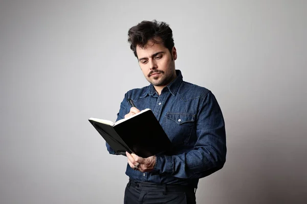 Joven hipster moderno con un libro y con una camisa de mezclilla con estilo. Chico atractivo en ropa de moda . — Foto de Stock