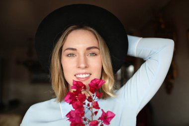 Kafkasyalı genç bir kadının keyfi yerinde, şapkası var ve elinde kır çiçekleri var..