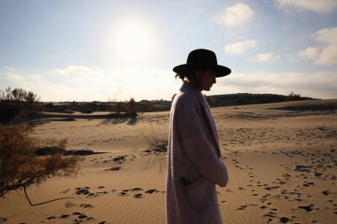 Çölde yürürken fötr şapka takan genç bir kadın. Yatay fotoğraf.