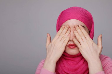 Başörtüsü takan, elini kaldırıp gözlerini kapatan genç bir müslüman kadının yakın plan portresi. Kadın hakları kavramı.