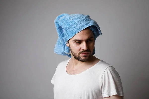 Uomo barbuto che indossa un asciugamano blu sulla testa e maglietta bianca, isolato su grigio, concetto di cura dei capelli . — Foto Stock