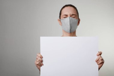 Tıbbi yüz koruma maskeli beyaz pankartlı genç bir kadının yakın plan portresi. Pandemik bir durum. Metin için boşluk.