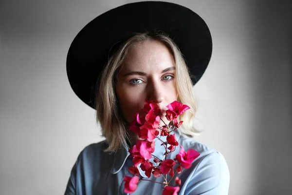 Menina bonita jovem em um segurando uma primavera flores florescentes. Estilo Boho. Mulher no chapéu fedora e camisa azul . — Fotografia de Stock