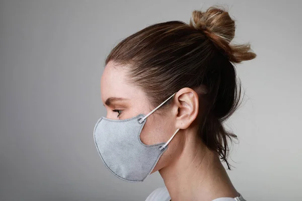 Side portrait of young woman in medical face protection mask indoors on white background. Protection of the virus.
