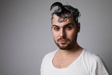 Mutlu sakallı, şaşırtıcı yüzlü ve gri arka planda ıslak saçlarla poz veren bir adam. Saç bakımı konsepti.